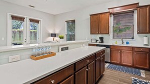 A modern kitchen with white countertops, wooden cabinets, a large island, and a built-in dishwasher. - Coconut Cove (Jacksonville Beach)