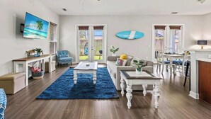 A spacious living room with a ceiling fan, a TV mounted on the wall, a blue rug, and a dining area with a table and chairs. - Coconut Cove (Jacksonville Beach)