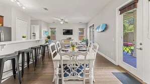 A dining area with a white table and chairs, a ceiling fan, and a kitchen area with a refrigerator and cabinets. - Coconut Cove (Jacksonville Beach)