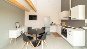 Una cuina moderna amb armaris blancs, forn integrat i una barra de bresca d'acer inoxidable.