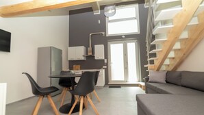 Un espai modern d'estar amb zona de menjador, un sofà gris i una escala.