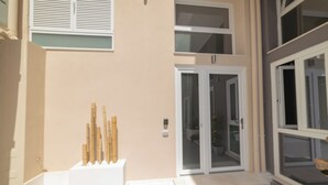 Entrada d'un edifici amb una porta blanca, un petit escaló que hi mena i una paret blanca amb un petit finestral sobre la porta.