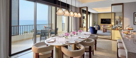 A dining area with a large round table set for six, a balcony with a view of the sea, and a modern kitchen in the background.