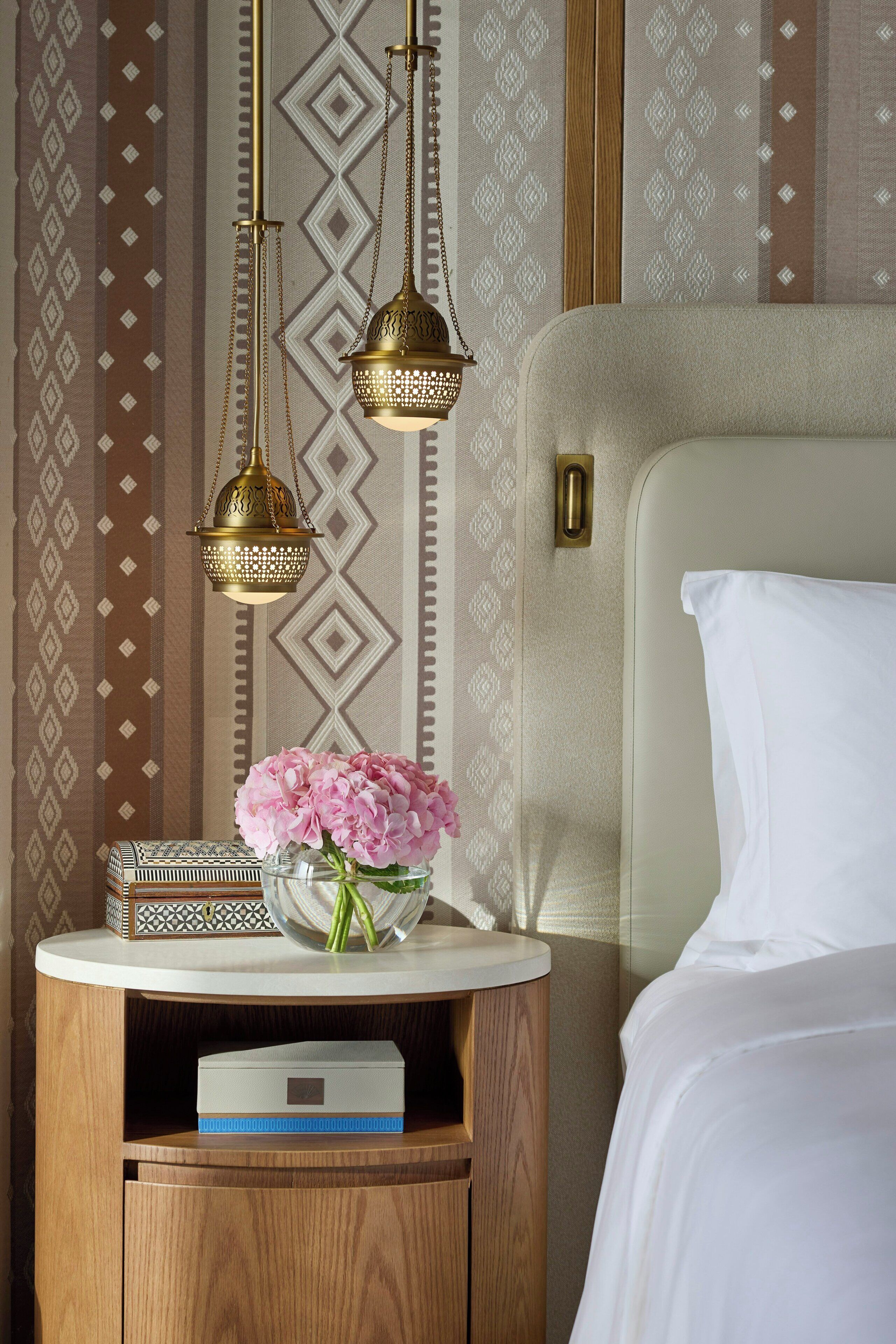 Une chambre d’hôtel bien rangée, avec un lit, une table de chevet dotée d’une lampe, un vase de fleurs et un papier peint à motifs.