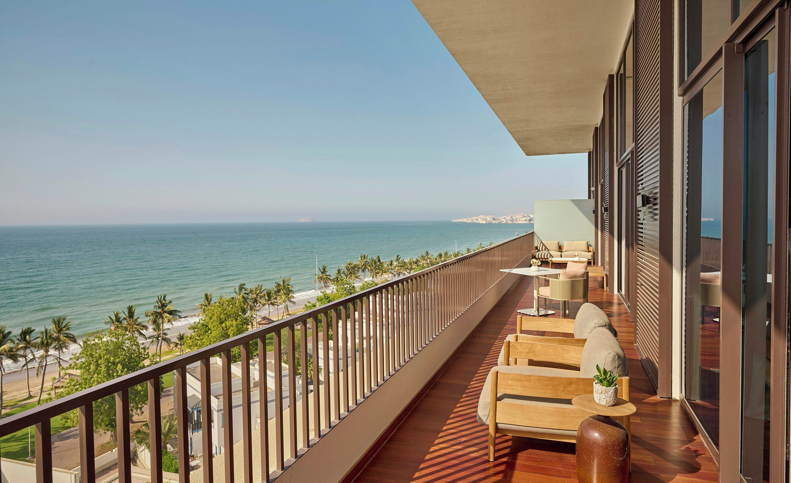 A balcony with a view of the ocean, wooden furniture, and a potted plant.