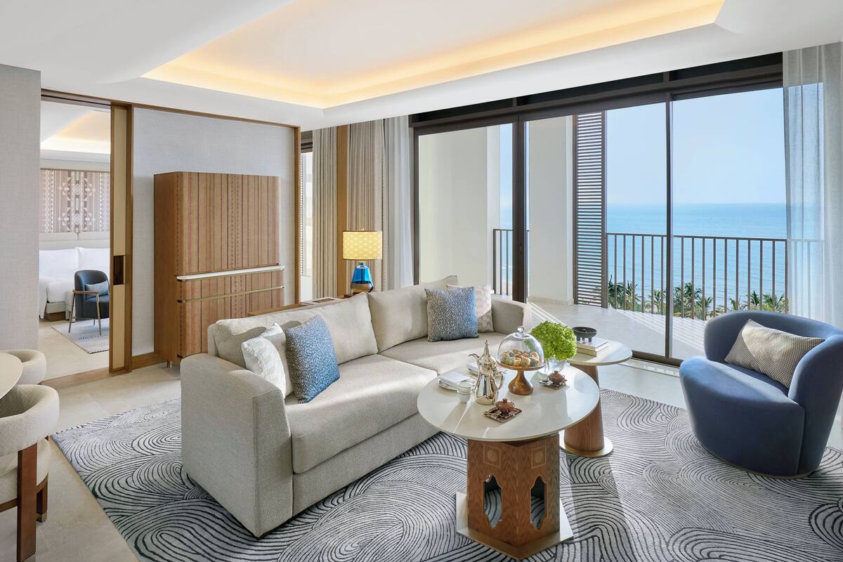 A modern hotel room with a large balcony, a sofa, a coffee table, and a chair.