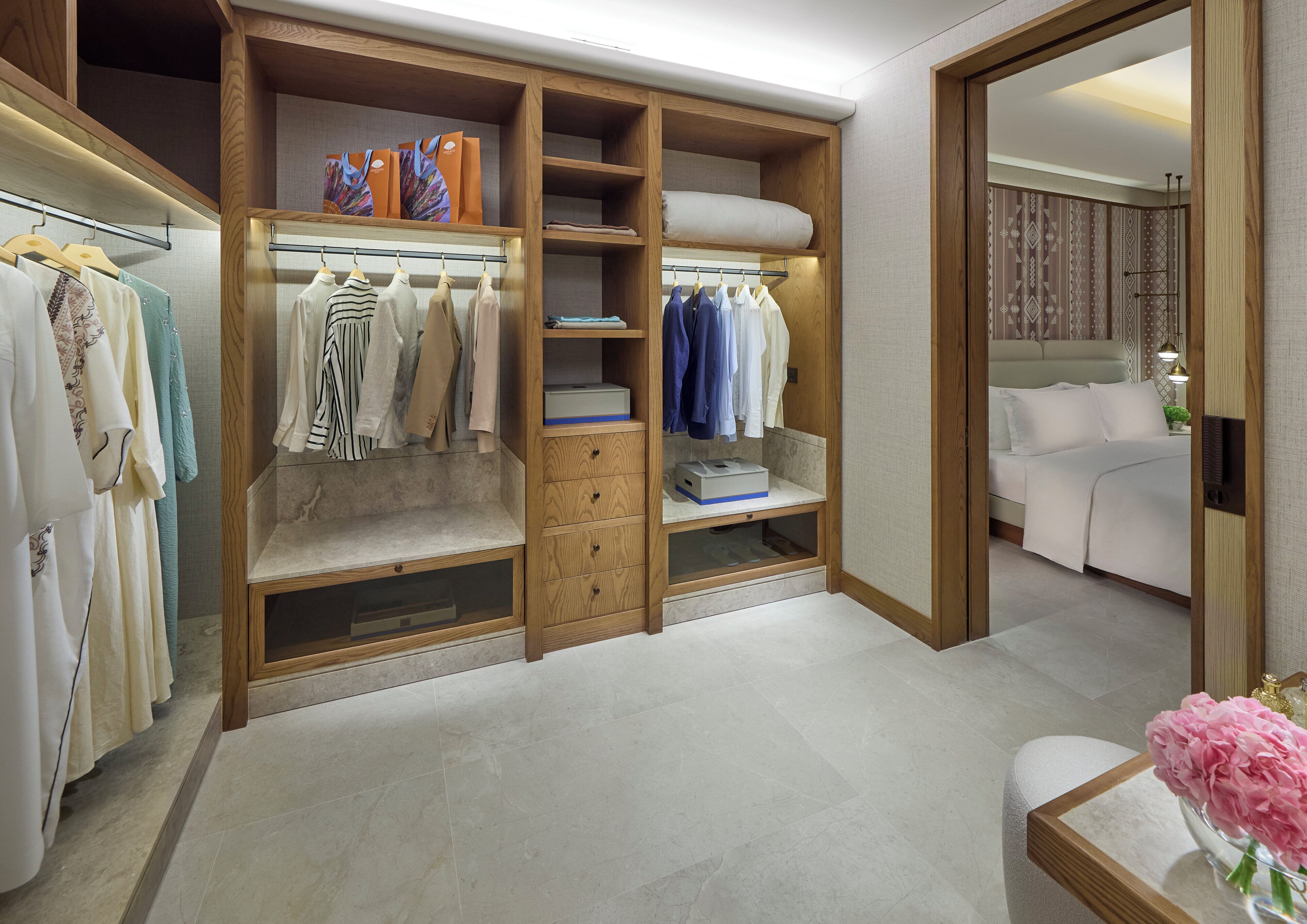A walk-in closet with multiple shelves and drawers, a bed, and a bathroom with a sink and mirror.