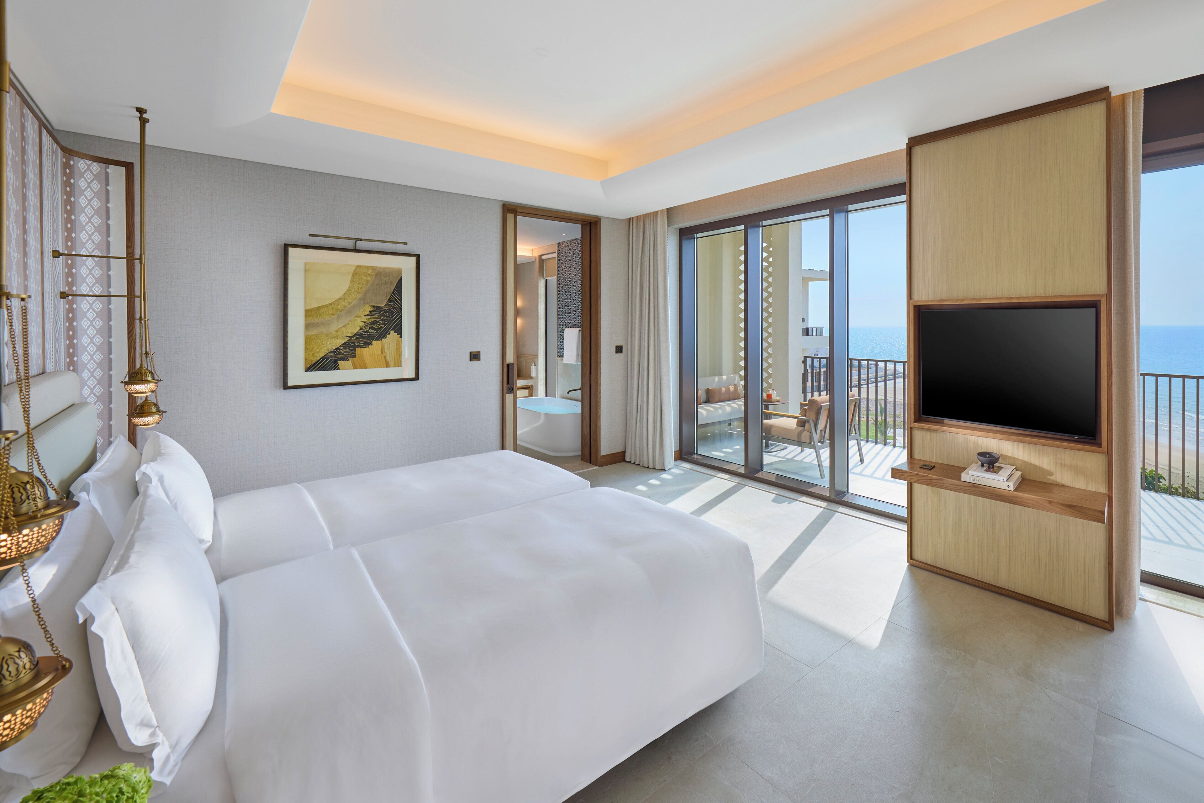 Una habitación de hotel moderna con una cama grande, un televisor de pantalla plana y un balcón con vistas al mar.