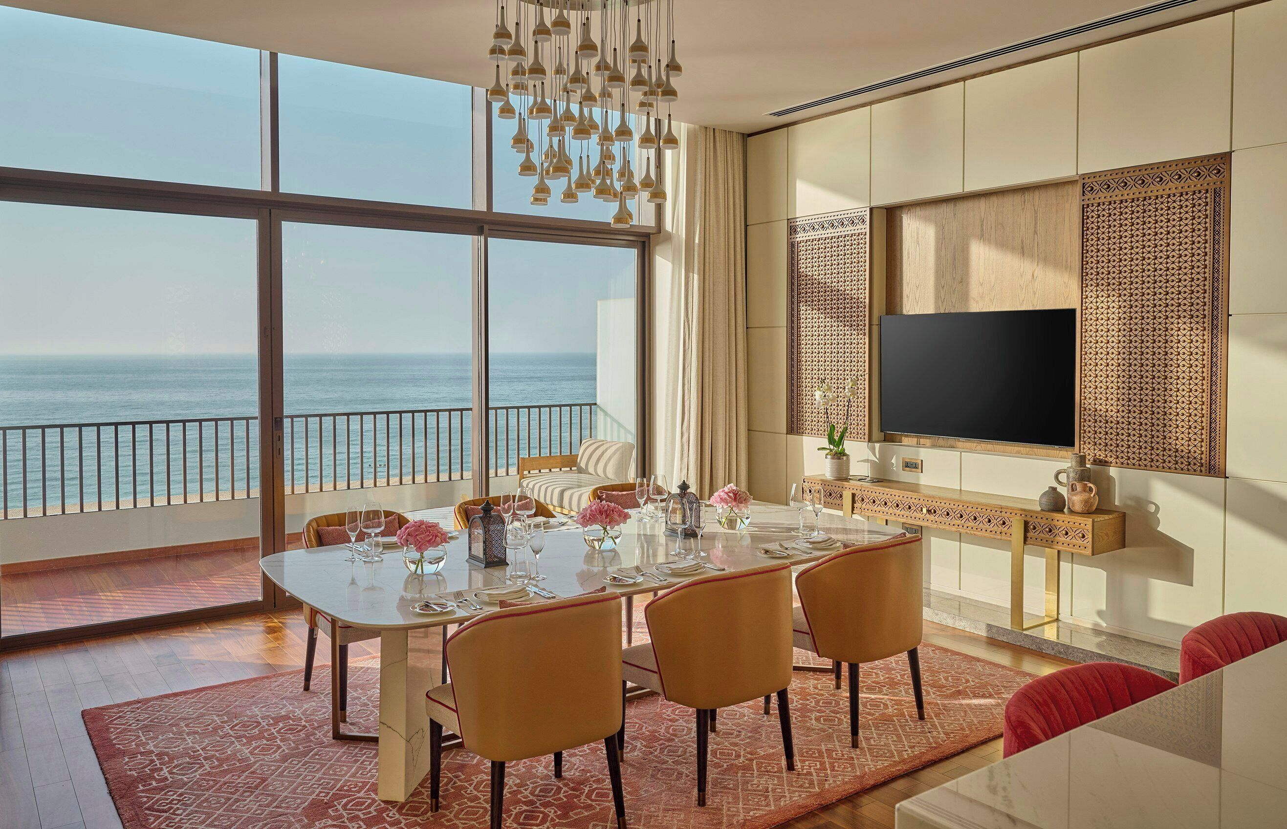 Un comedor con una mesa grande dispuesta para seis, un televisor montado en la pared y vista al océano.