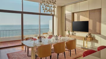 Un comedor con una mesa grande dispuesta para seis, un televisor montado en la pared y vista al océano.
