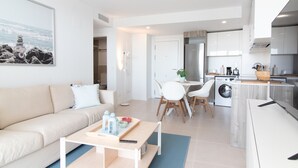 Un apartamento moderno con sala de estar, comedor y cocina. Cuenta con un sofá, mesa de comedor, sillas, cafetera y lavadora.