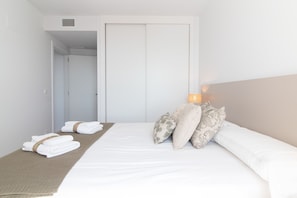 A hotel room with a neatly made bed, a bedside lamp, and a set of towels on the floor.