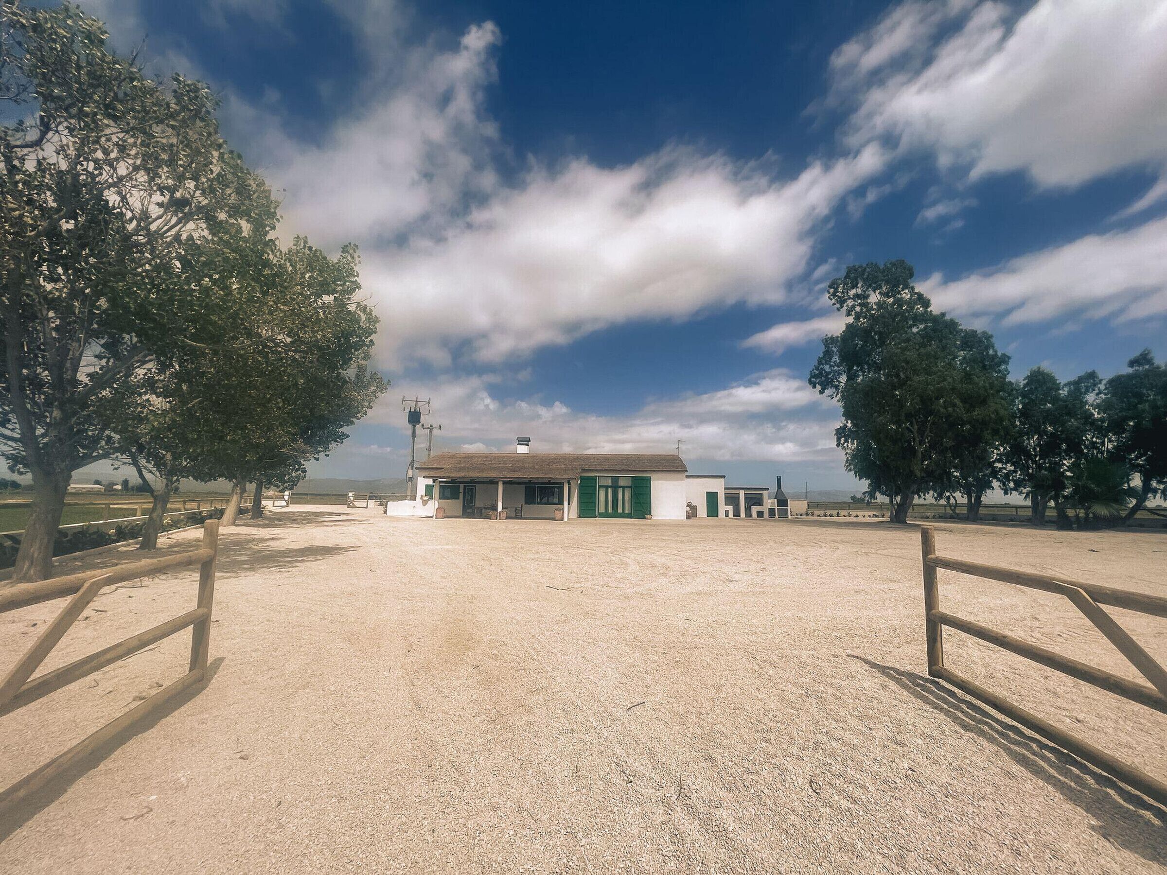 A stable with a dirt floor, surrounded by trees and a clear sky.