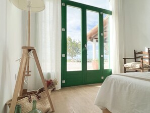 A room with a bed, a chair, a lamp, and a view through green doors.