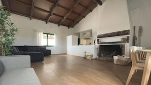 A spacious living room with a fireplace, a sofa, a dining table, and a large window. - Idyllic Rural Retreat: Spacious 4BR House, BBQ, Wi-Fi, Near Beaches & Delta Wildlife Reserve (Deltebre)