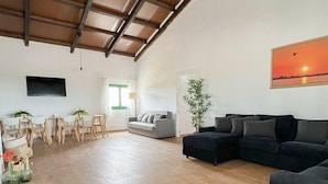 A spacious living area with a wooden floor, a grey sofa, a black sofa, a dining table with chairs, and a large window with curtains. - Idyllic Rural Retreat: Spacious 4BR House, BBQ, Wi-Fi, Near Beaches & Delta Wildlife Reserve (Deltebre)