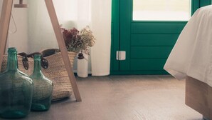 A room with a green door, a wooden floor, and a bed with white bedding. There are two green glass bottles and a woven basket with dried flowers. - Idyllic Rural Retreat: Spacious 4BR House, BBQ, Wi-Fi, Near Beaches & Delta Wildlife Reserve (Deltebre)