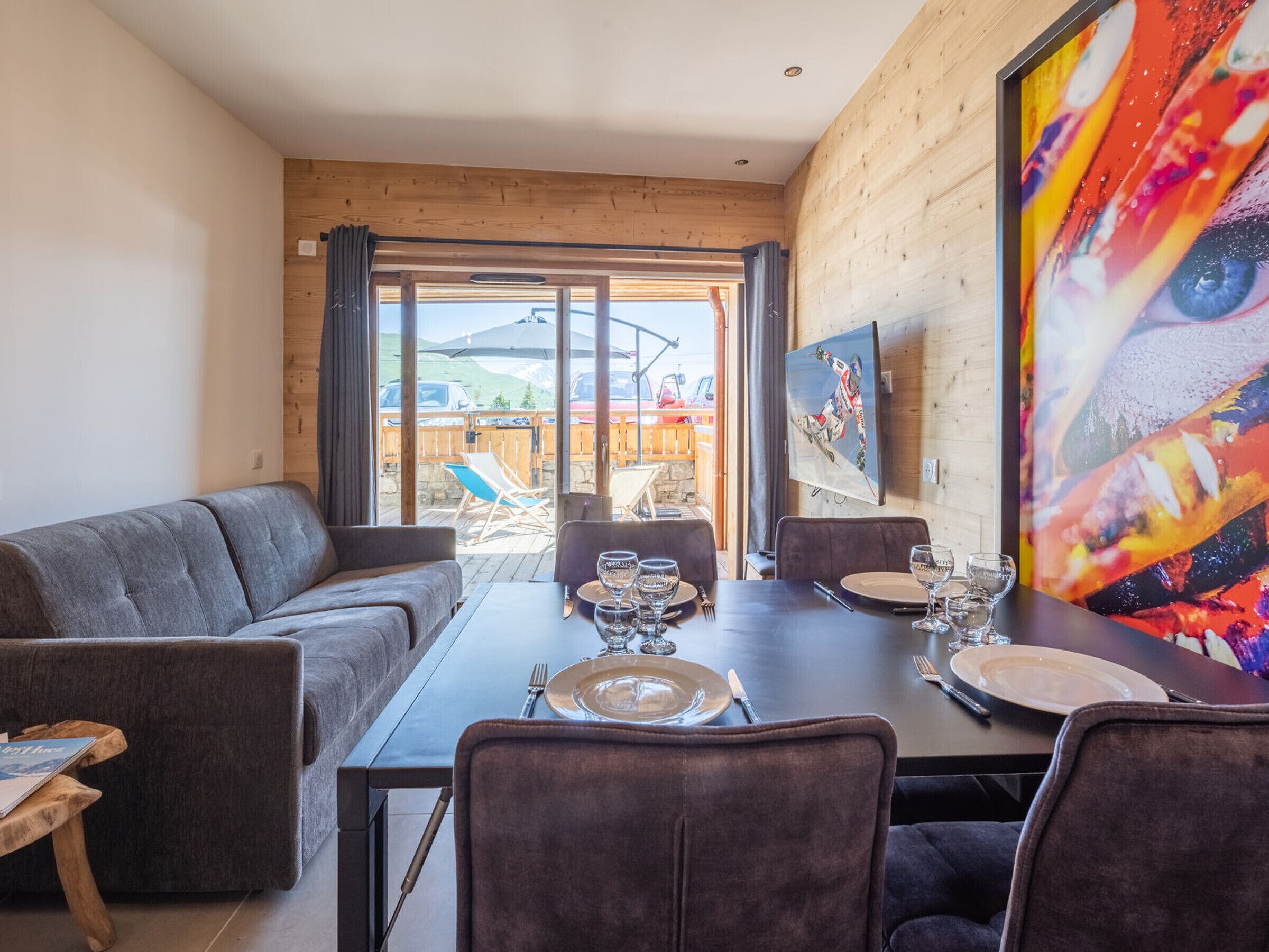 A dining area with a wooden table set for four, a grey sofa, and a large painting on the wall.
