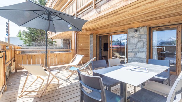 Une terrasse en bois avec une table et des chaises, un grand parasol et un mur en pierre.
