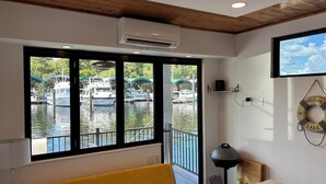 Una habitación con un ventanal grande con vistas a un puerto deportivo, una banca, un lavabo y un aire acondicionado de pared.