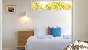 Une chambre à coucher avec une tête de lit en bois, un lit avec une literie blanche et des oreillers bleus, une lampe de chevet et un tableau encadré au mur.