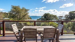 Une terrasse en bois avec une table et des chaises, offrant une vue panoramique sur des arbres et une étendue d’eau.