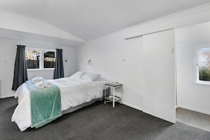 A bedroom with a bed, a bedside table, a window, and a door.