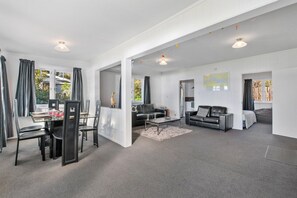 A modern living room with a dining area, grey carpet, and a view of the outdoors.