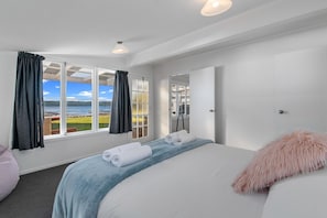 A hotel room with a large bed, a view of the sea, and a window with curtains.
