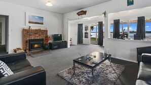 A modern living room with a fireplace, black leather sofas, a glass coffee table, and a view of the sea through large windows.