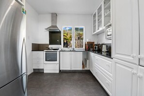 A modern kitchen with white cabinetry, a stainless steel refrigerator, a built-in oven, and a window with a view of greenery.