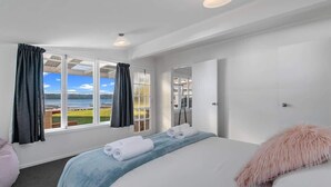 A hotel room with a large bed, a view of the sea, and a window with curtains.