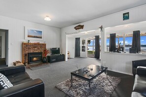 A living room with a fireplace, a television, and a view of the outdoors. - The Middle - Lakefront + Jetty, Sleeps 8 (Rotoiti Forest)