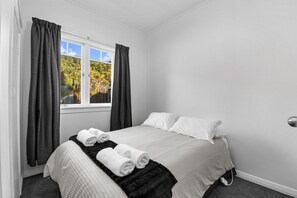 A hotel room with a bed, two pillows, a window with curtains, and a view of trees. - The Middle - Lakefront + Jetty, Sleeps 8 (Rotoiti Forest)