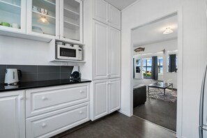 A modern kitchen with white cabinetry, a black countertop, and a microwave. There is a view into a dining area with a table and chairs. - The Middle - Lakefront + Jetty, Sleeps 8 (Rotoiti Forest)
