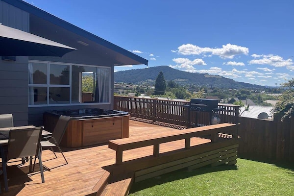 Elevated timber deck with spa pool and panoramic Rotorua hill views — ideal outdoor entertaining for holiday stays
