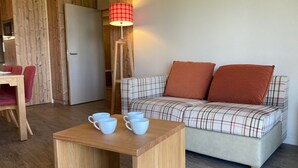 Una habitació acollidora amb un sofà escocès, una taula de fusta amb tasses, una làmpada i una porta de fusta.