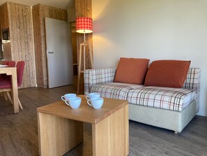 Une pièce chaleureuse avec un canapé à carreaux, une table en bois sur laquelle sont posées des tasses, une lampe et une porte en bois.