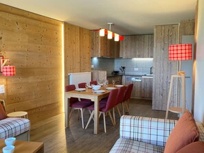 A modern kitchen with wooden cabinetry, a dining area with a table set for four, and a cozy seating area with a sofa and chairs.