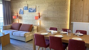 Una habitació acollidora amb sofà, taula de dinar i cadires, parets de fusta i una finestra amb cortines.