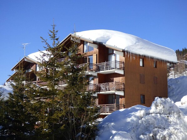 A multi-story wooden building with balconies, surrounded by snow and trees.