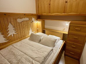 A wooden bunk bed with a headboard featuring cut-out animal shapes, a bedside table with a lamp, and a wooden dresser with drawers.