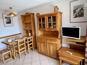 A wooden dining area with a table set for four, a television on a stand, and a cabinet with glass doors.