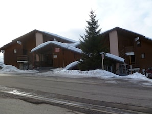 A two-story wooden building with a covered entrance and a sign indicating danger. Snow is piled up in front of the building.