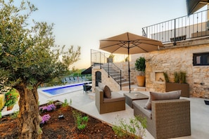 An outdoor patio area with wicker furniture, a stone wall, and a pool. - Casa Mar | Villa with Pool & Sea View in Porec (Mugeba)