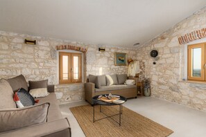 A room with stone walls, a sofa, a wicker chair, a round table, and a window with a view. - Casa Mar | Villa with Pool & Sea View in Porec (Mugeba)