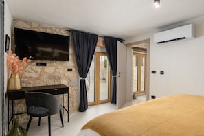 A bedroom with a bed, a desk with a chair, a TV, and a stone wall. - Casa Mar | Villa with Pool & Sea View in Porec (Mugeba)