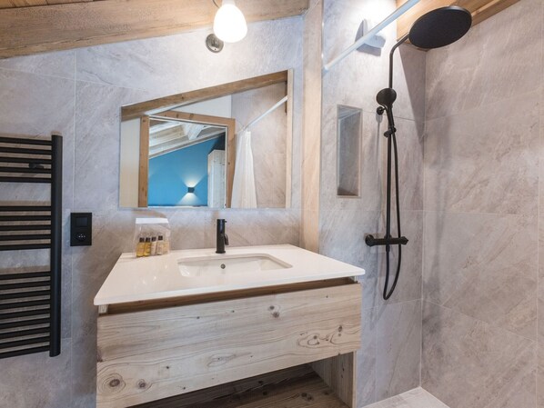 A modern bathroom with a white sink, wooden vanity, a mirror, and a shower with a handheld showerhead.