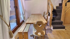 Una mesa de comedor de madera con bancos, un televisor montado en la pared y una escalera con barandillas de madera.