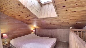Un dormitorio con techo inclinado, paredes de madera, una cama, dos lámparas de noche y un tragaluz.